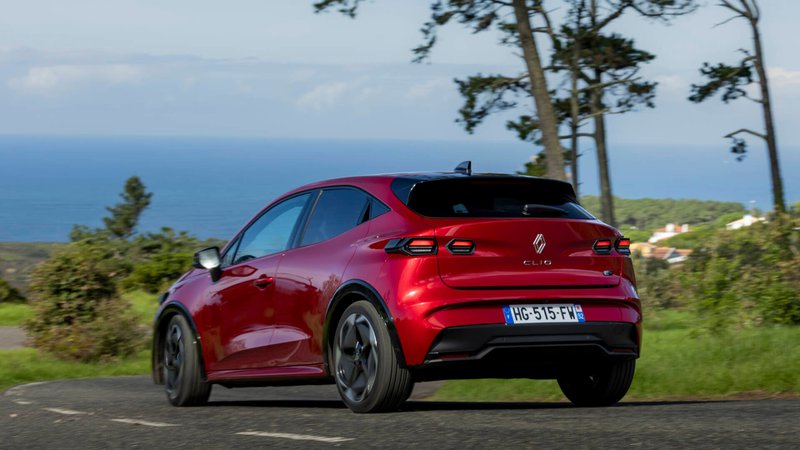 Renault Clio rouge vue de trois quarts arrière, en mouvement sur une route côtière avec la mer en arrière-plan.