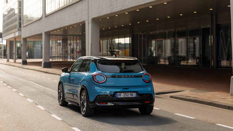 Micra électrique vue de l’arrière en circulation dans une rue bordée de bâtiments modernes.