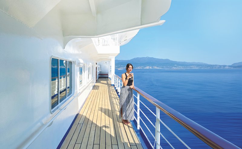 Dame met glas in de hand aan de reling van een schip uitkijkend op een blauwe zee - CroisiEurope