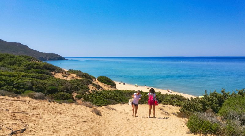 twee kinderen op een rustig strand met azuurblauw water en staalblauwe hemel - vliegvakantie Sardinië