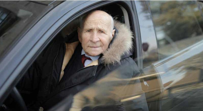 Un homme âgé vêtu d'un manteau d'hiver monte dans la voiture et regarde l'objectif.