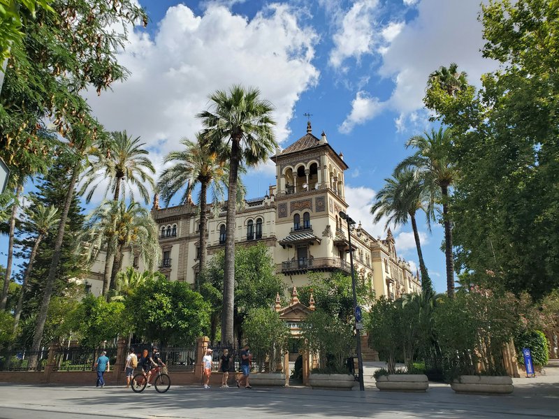 Cruise in Andalusië: mensen lopen overdag op straat bij een beige betonnen gebouw tussen de palmbomen