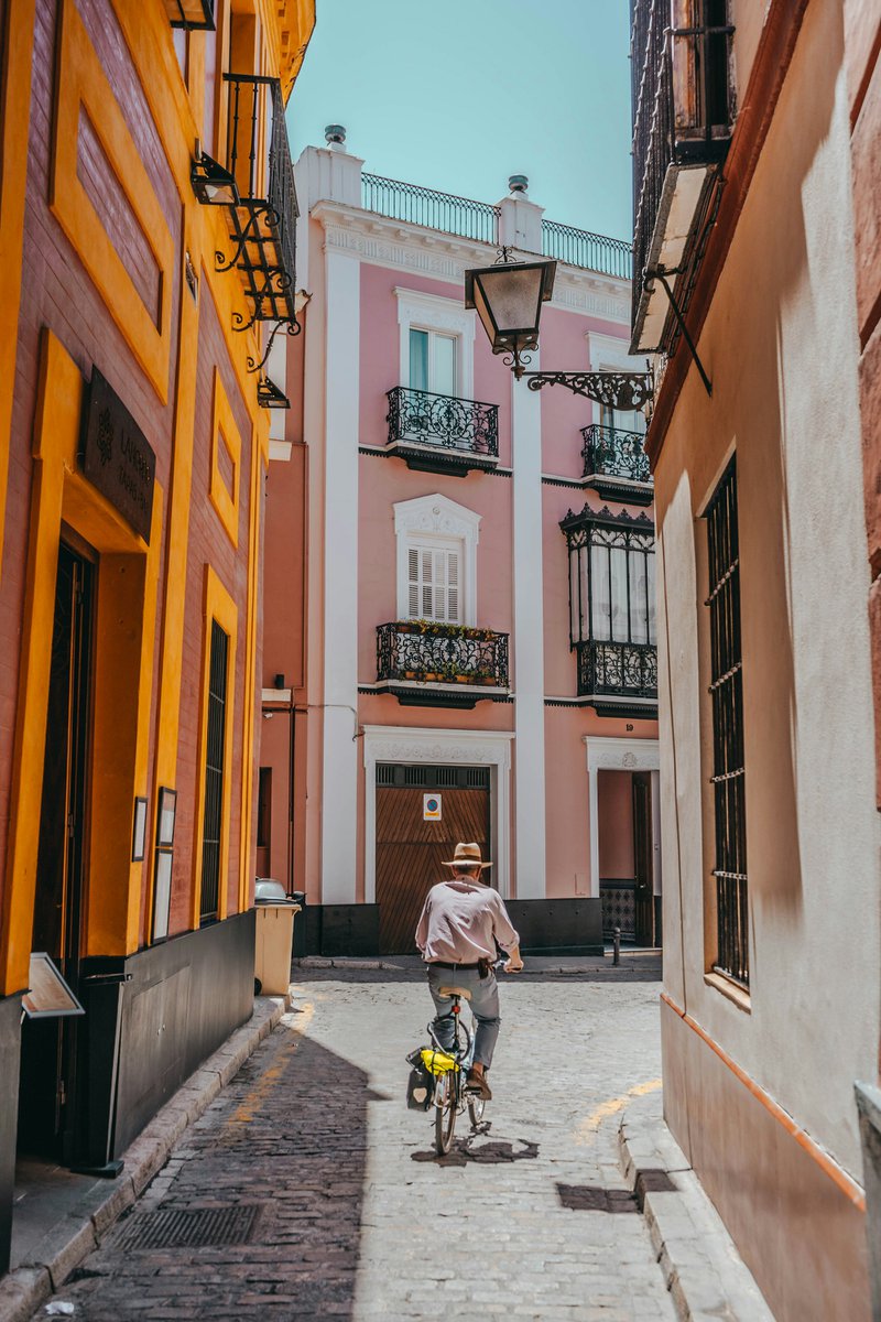 cycliste dans une ruelle étroite bordée de maisons colorées à Séville.