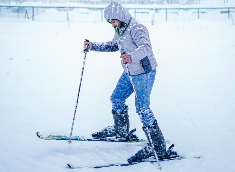 Homme en train de skier en jeans sous la neige.