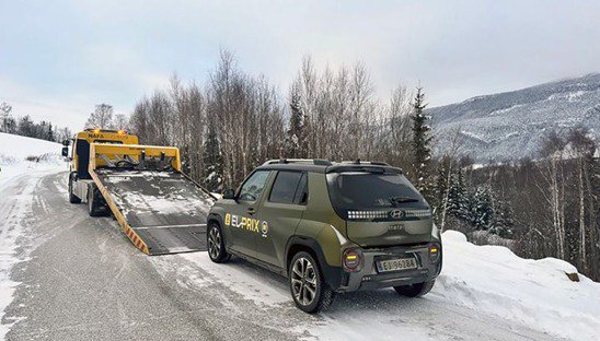 Une Hyundai Inster verte est chargée sur un camion dans un paysage enneigé.