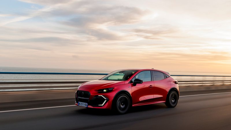 Renault Clio rouge en mouvement sur une route en bord de mer au coucher du soleil, vue de trois quarts avant.
