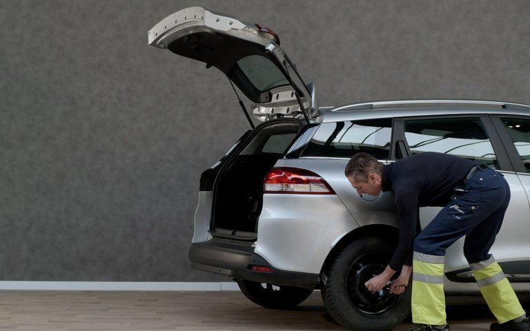 man vervangt band van grijze auto