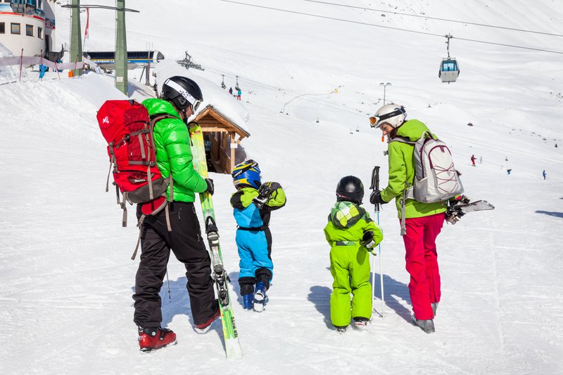 Deux parents sur les pistes de ski avec leurs deux jeunes enfants.