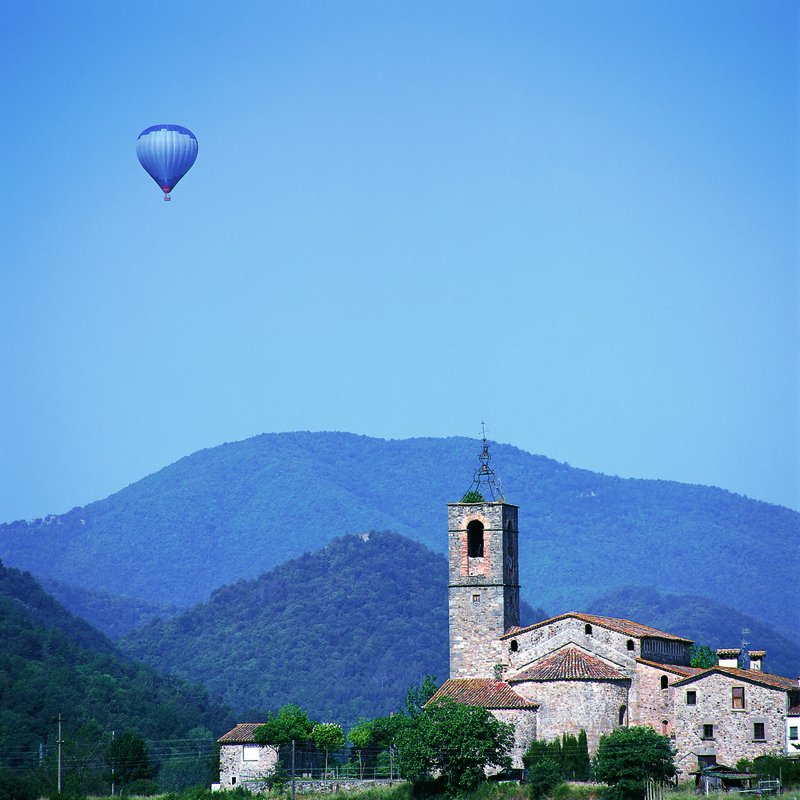 Montgolfière bleue dans un ciel bleu survolant un village de montagne avec une église romane.