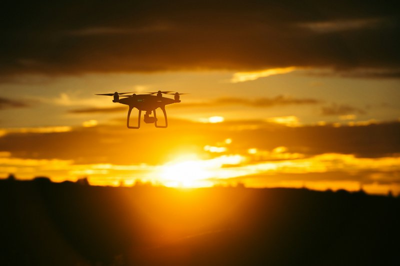 Drone vliegt in de lucht, met de ondergaande zon op de achtergrond.