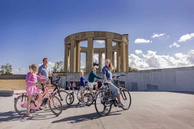 Familie fietsers aan groot bouwwerk onder een blauwe hemel