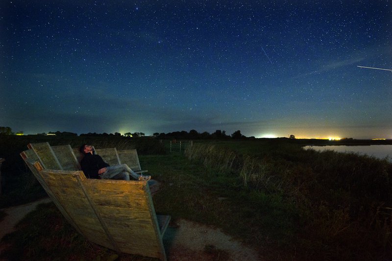man kijkt in het donker vanuit een houten zitting naar de sterrenhemel in Friesland