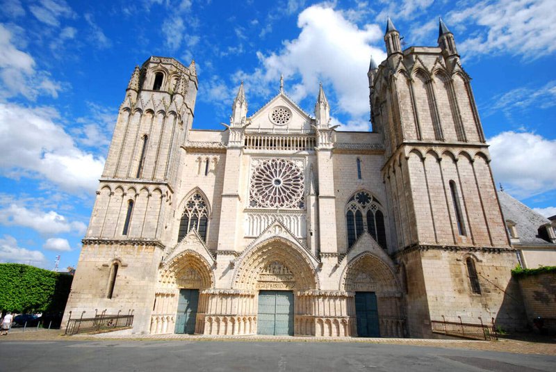 Façade d'une cathédrale de style roman avec des éléments gothiques, ciel bleu en arrière-plan.