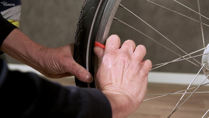 Une main retire un pneu de vélo avec un outil.
