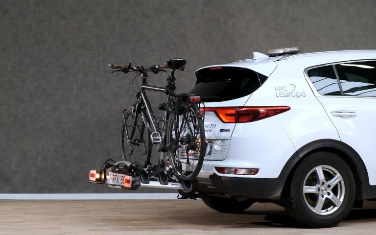 porte-vélos avec 1 vélo, fixé sur l'attelage d'une voiture blanche.