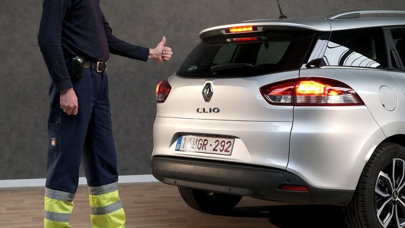 Un homme fait le signe du pouce levé à l'arrière d'une voiture grise.