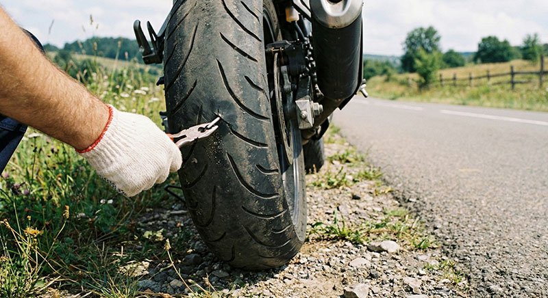 Close-up van lekke motorband met nagel die wordt verwijderd tijdens pechverhelping langs de weg