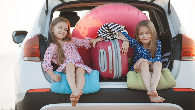 Deux petites filles assises dans le coffre avec une valise. Illustration pour dire l'importance du chargement des bagages avant de prendre la route.