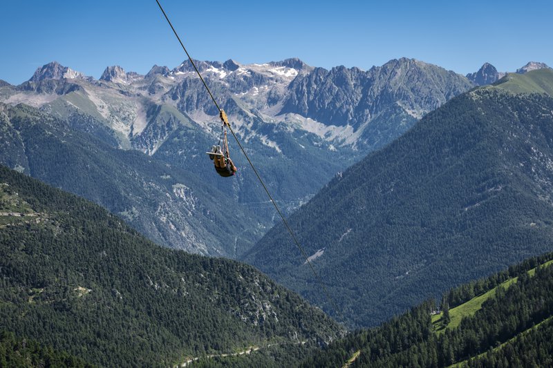 personne en train de descendre sur une tyrolienne, montagnes en arrière-plan