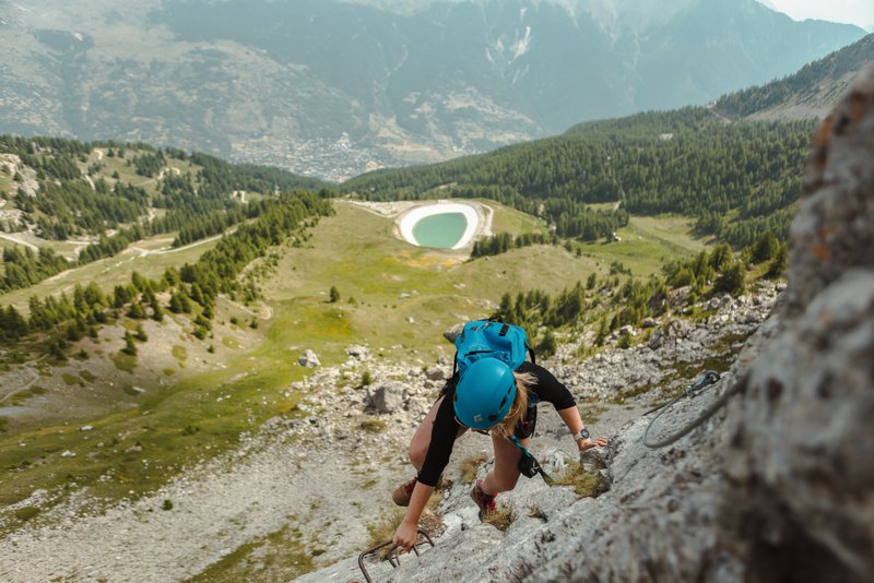 personne escaladant un rocher avec des montagnes en arrière-plan et un lac en contrebas