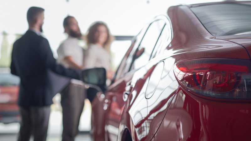 Tweedehands: achterkant van een rode auto in een showroom, klanten die op de achtergrond staan te praten.