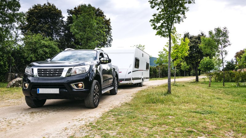 een zware pick-up trekt een grote caravan over een onverharde weg