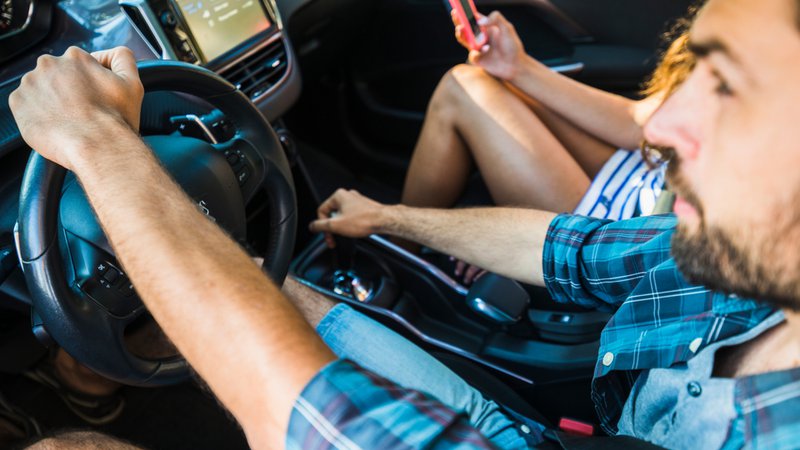Een bestuurder die tijdens een autorit de airconditioning instelt, met een passagier naast zich.