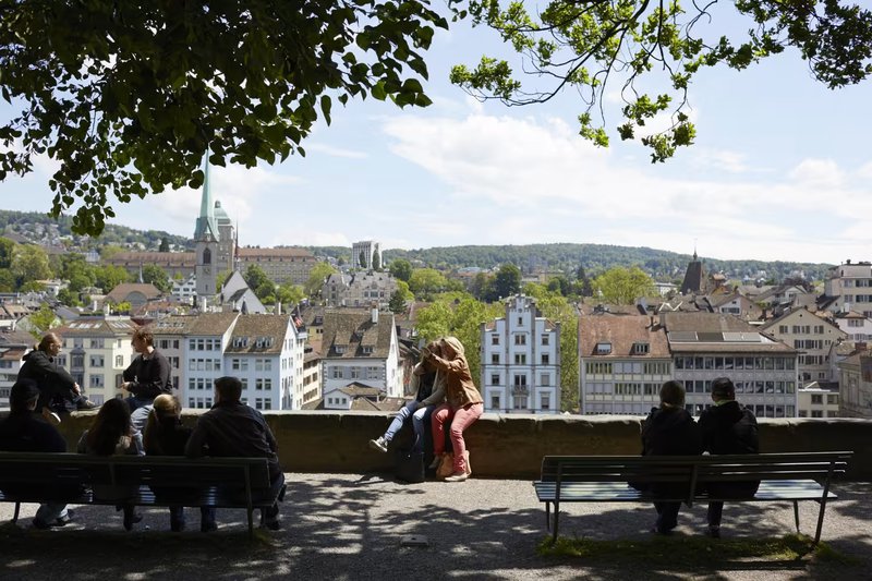koppeltje en mensen op banken die uitkeken over de daken van een lagergelegen stad