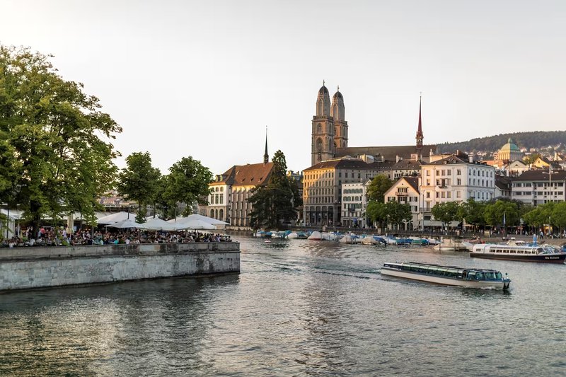 terrasjes aan het water met bootjes en op de achtergrond een statige kerk met 2 torens - Zürich